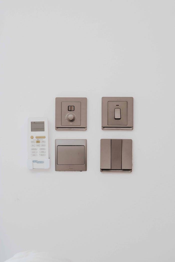 A clean, minimalist arrangement of a remote control and four light switches against a white wall.