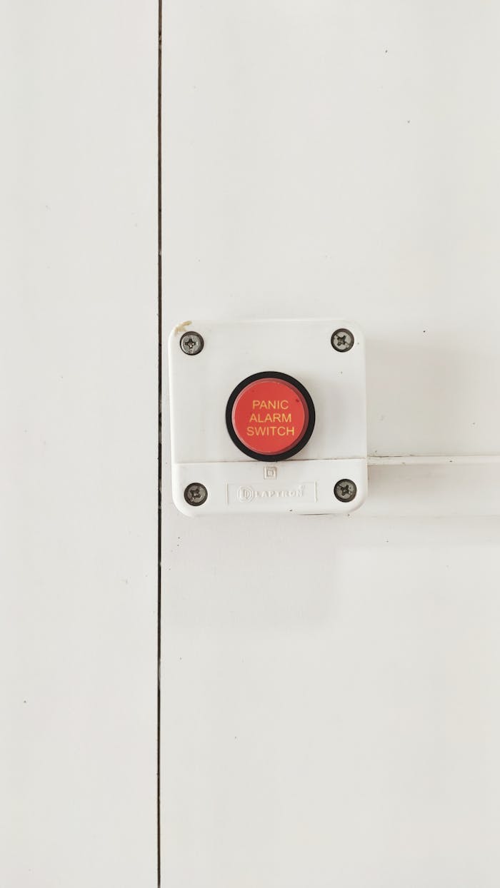 A red panic alarm switch mounted on a clean white wall, emphasizing safety measures indoors.